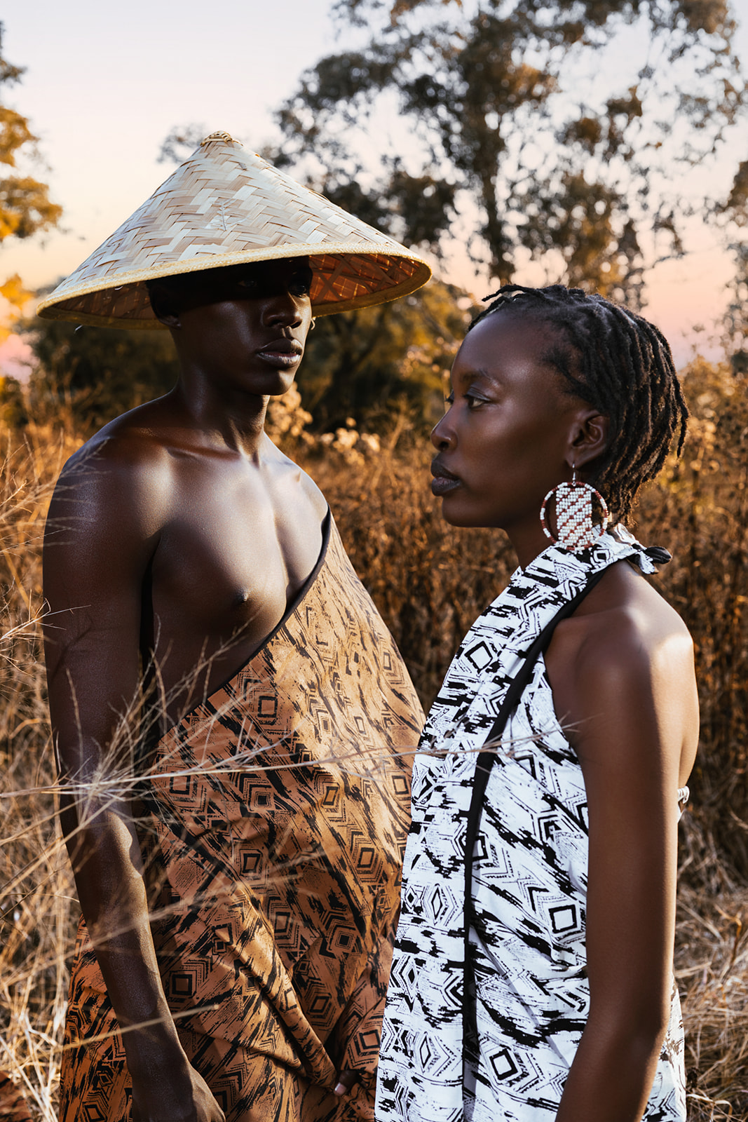 Model in white MOSI geometric print wrap and conical hat, golden grassland sunset backdrop.