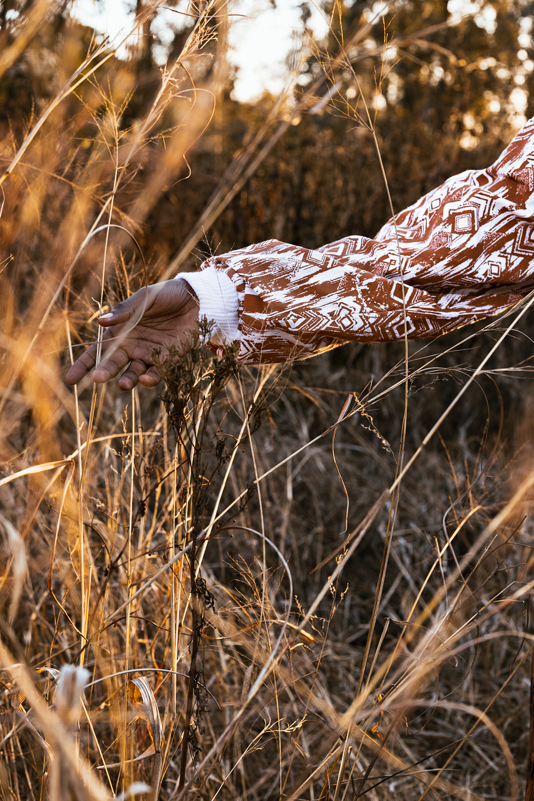 Model's hand holding ochre-and-white MOSI print fabric in dry grasses at golden hour.