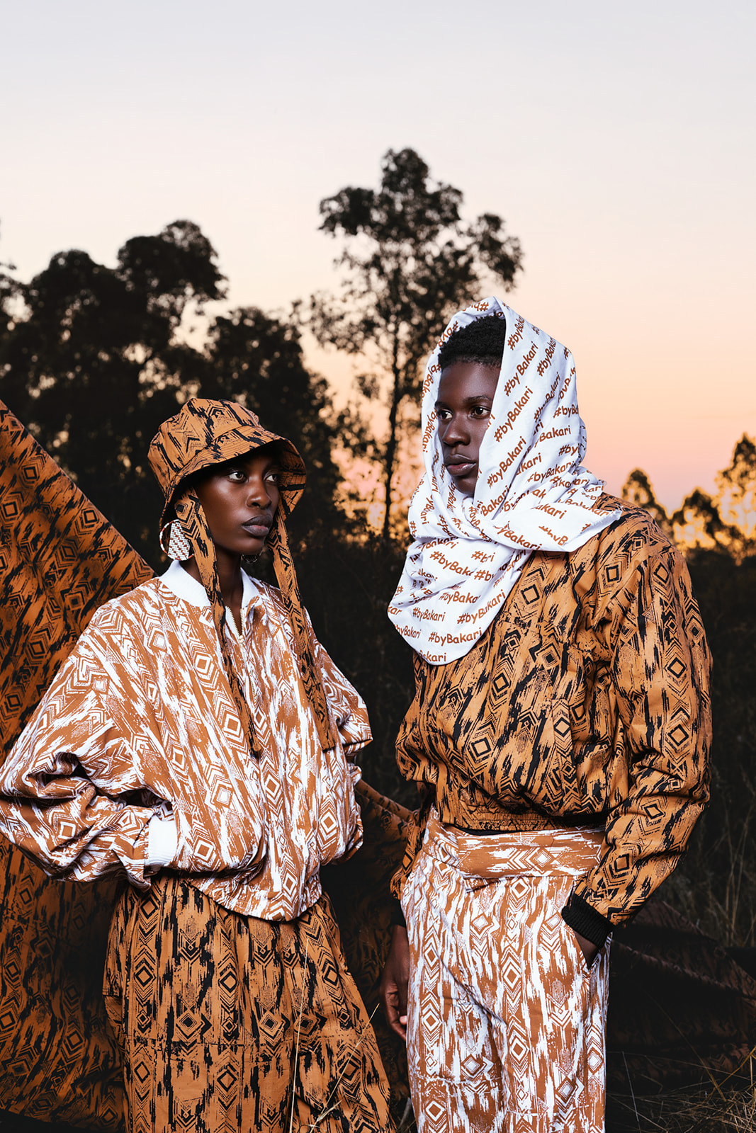 Two models in coordinating MOSI prints, one headwrapped, against natural landscape at dusk.