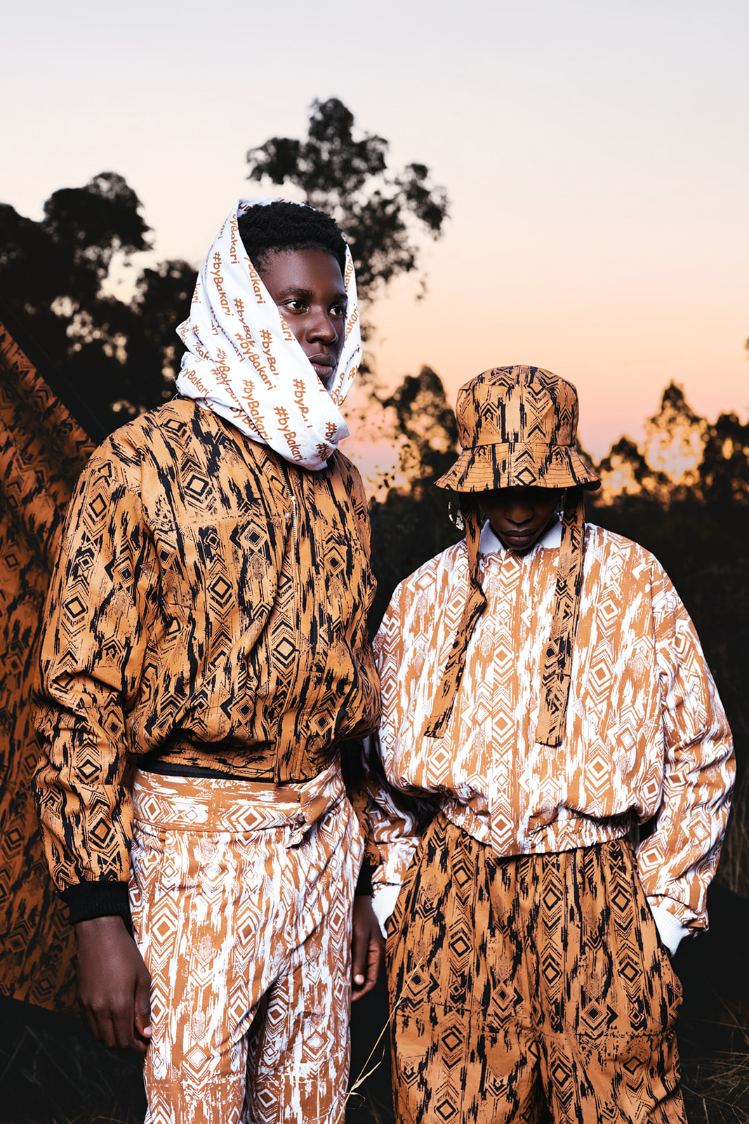 Two models in white and ochre MOSI prints converse outdoors at golden-hour sunset.